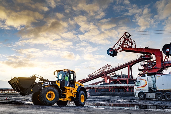 JCB 457S wheel loader working at an industrial facility alongside conveyor equipment