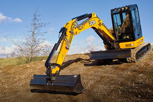 JCB 50Z-1 mini excavator grading soil on sloped ground with front dozer blade