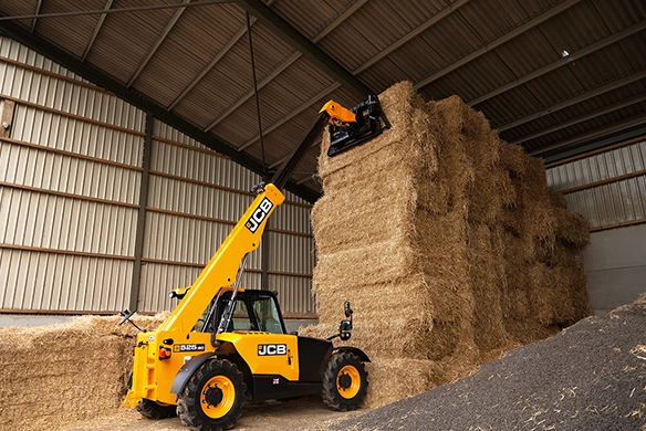 JCB 525-60 telescopic handler stacking hay bales at height inside a barn