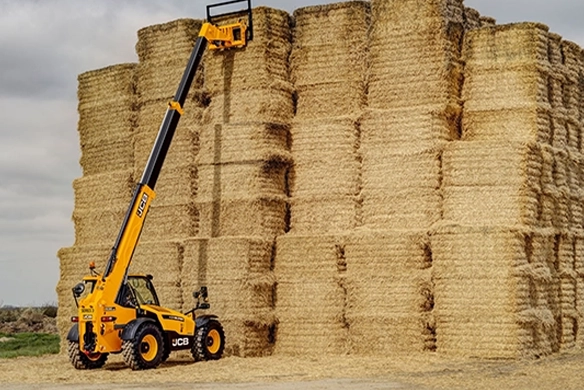 JCB 536-95 telescopic handler stacking large hay bales at height in an agricultural yard
