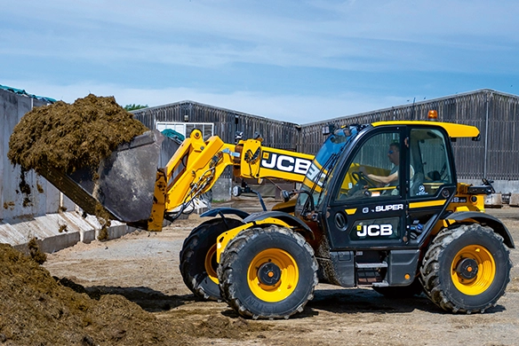 JCB 538-60 Agri carrying a full silage bucket between farm buildings