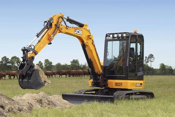 JCB 55Z-1 mini excavator digging soil on agricultural land with livestock in the background