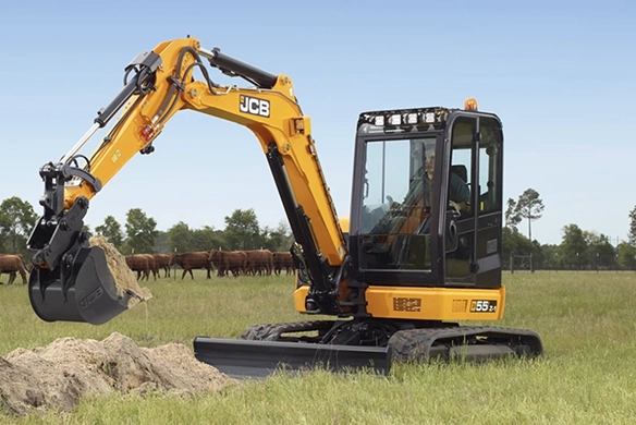 JCB 55Z-1 mini excavator digging soil on agricultural land with livestock in the background