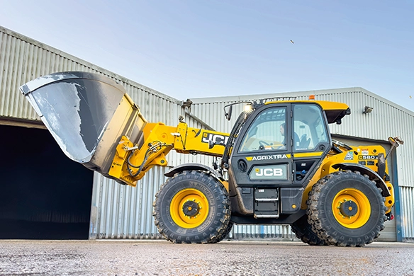 JCB 560-80 telescopic handler with grain bucket raised outside an agricultural shed