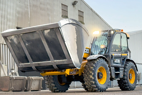 Front view of JCB 560-80 telescopic handler carrying a large high-capacity bucket on concrete yard