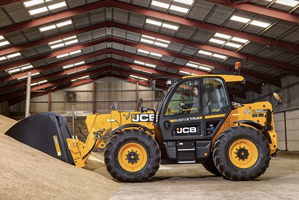 JCB 560-80 telescopic handler loading grain inside a steel-framed farm building