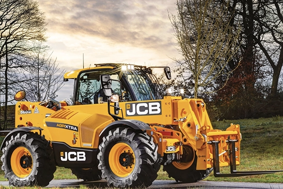 Front three-quarter view of JCB 560-80 telescopic handler fitted with fork carriage at sunset