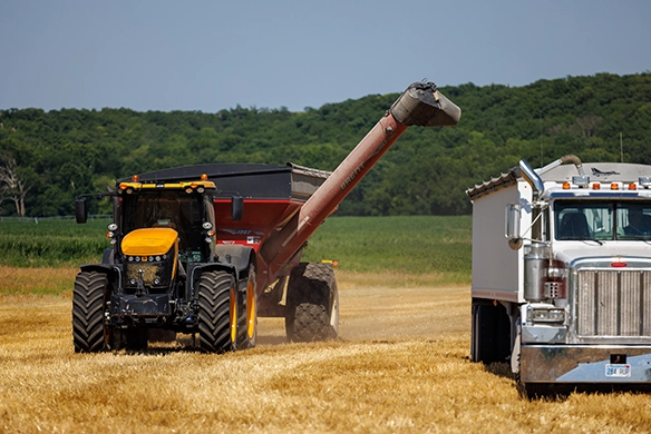 JCB 8000 Series tractor unloading grain into a highway truck during harvest