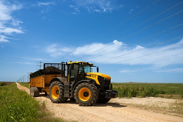 JCB 8000 Series tractor towing a loaded trailer on a rural gravel road