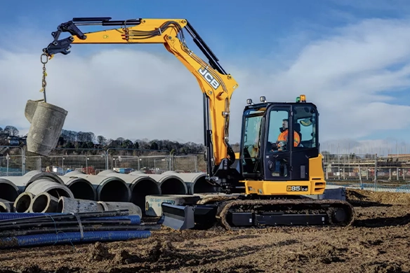 JCB 85Z-1 mini excavator lifting concrete pipes on a construction site