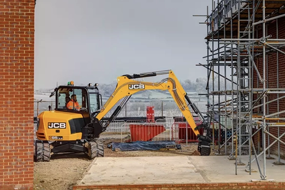 JCB 85Z-1 mini excavator operating close to scaffolding on an urban construction site