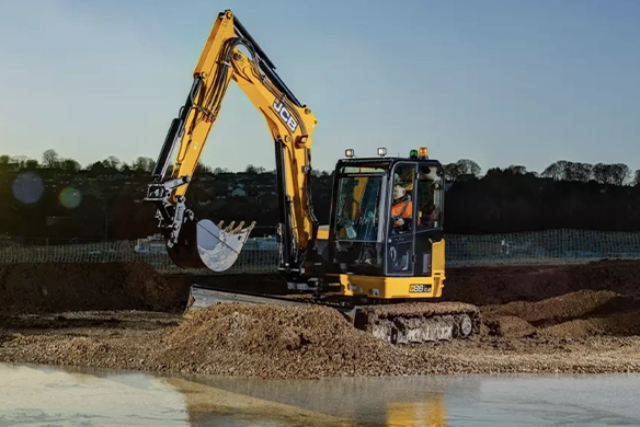 JCB 86C mini excavator excavating soil near a water feature during groundworks on a construction site