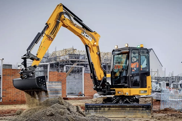 JCB 86C mini excavator loading material on a construction site with masonry and scaffolding in the background