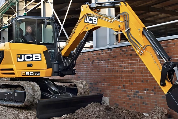 JCB 90Z-2 mini excavator excavating soil alongside a brick wall on a construction site