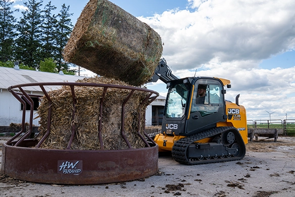 JCB 270T compact track loader handling round hay bales on a farm