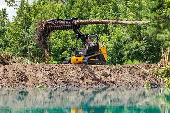 JCB 300T compact track loader lifting a large tree trunk during land clearing near water