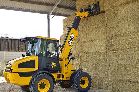 JCB TM220 telescopic wheel loader stacking straw bales inside an agricultural storage building
