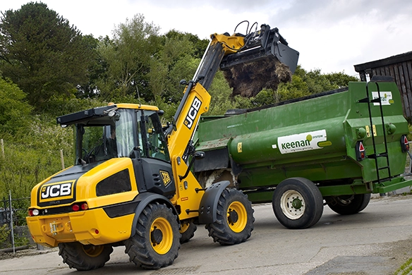 JCB TM220 telescopic wheel loader loading material into a feeder wagon on a farm