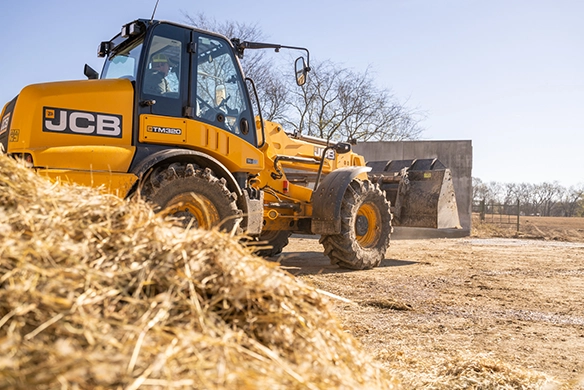JCB TM320 telescopic wheel loader working in a farm yard with straw and bedding material