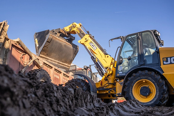 Low-angle view of JCB TM320 telescopic wheel loader tipping material into a farm trailer