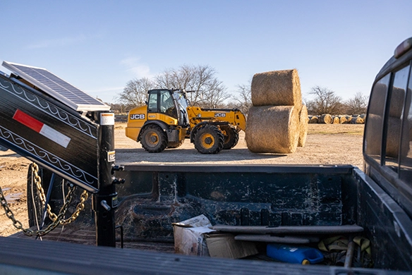 JCB TM320 telescopic wheel loader transporting large straw bales across an agricultural site