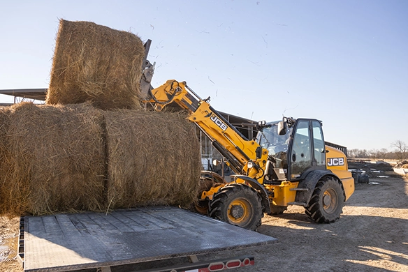JCB TM320 telescopic wheel loader loading stacked straw bales onto a flatbed trailer