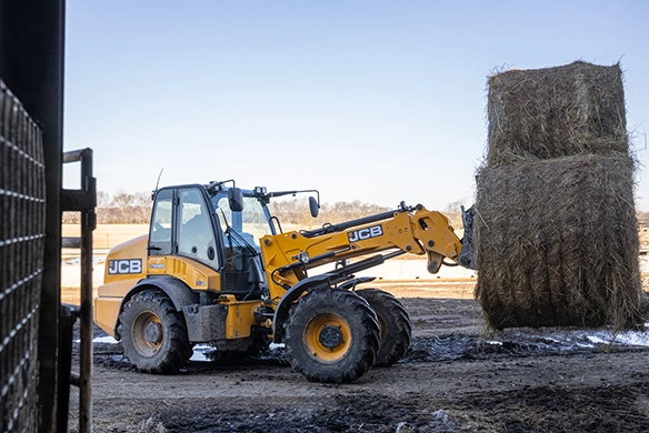 JCB TM320 telescopic wheel loader positioning straw bales during farm material handling
