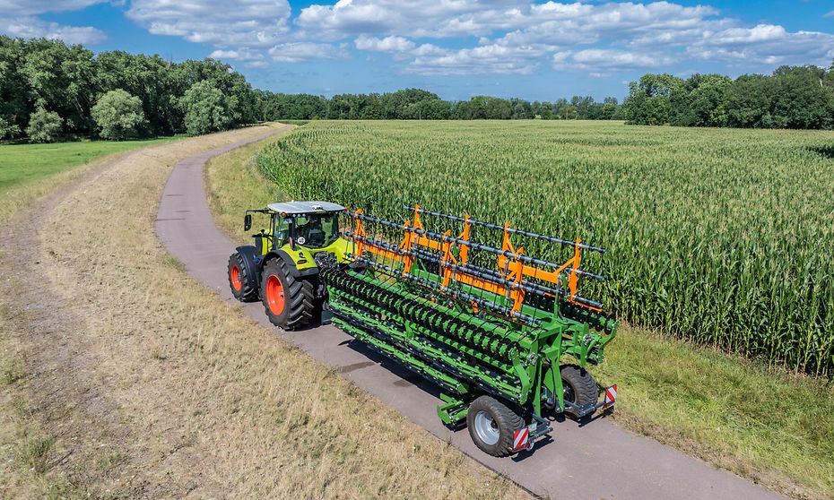 12m TopCut folded and being transported with a tractor through a crop field.